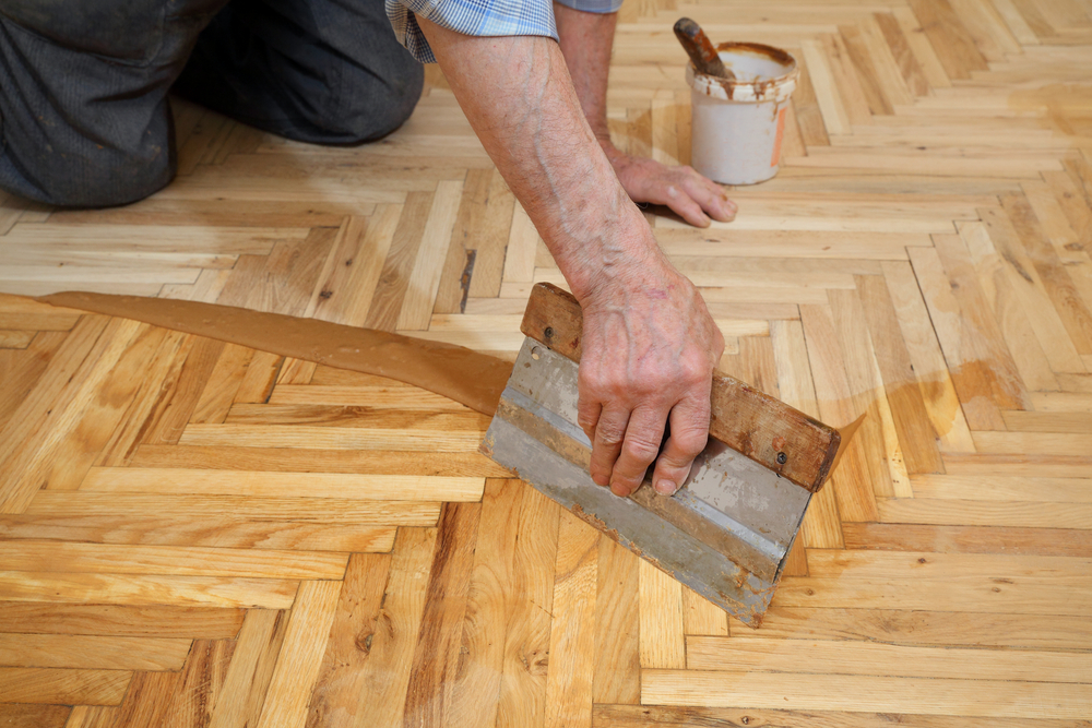 A craftsman applying a wood filler across a newly sanded herringbone oak parquet floor, emphasizing the wood floor sanding process and surface preparation.