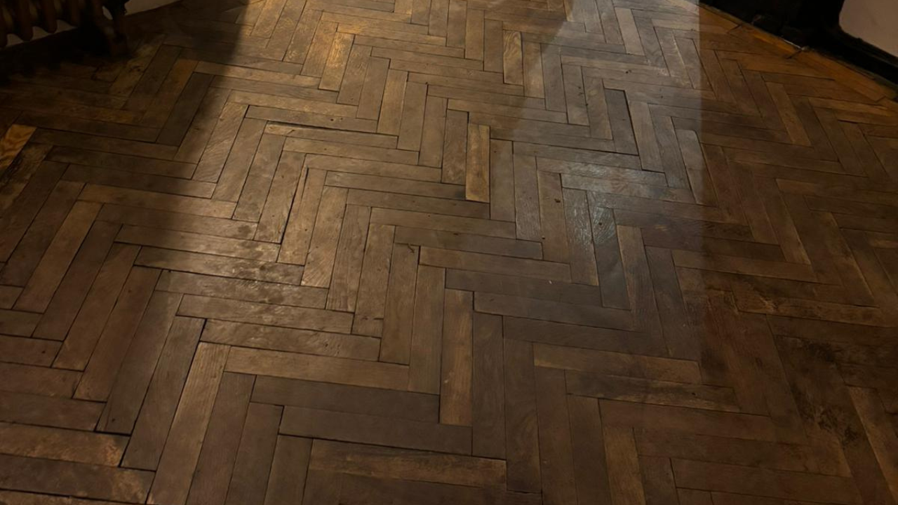 A dark and worn herringbone parquet floor, showing signs of wear and discoloration, illustrating the need for professional wood floor sanding.