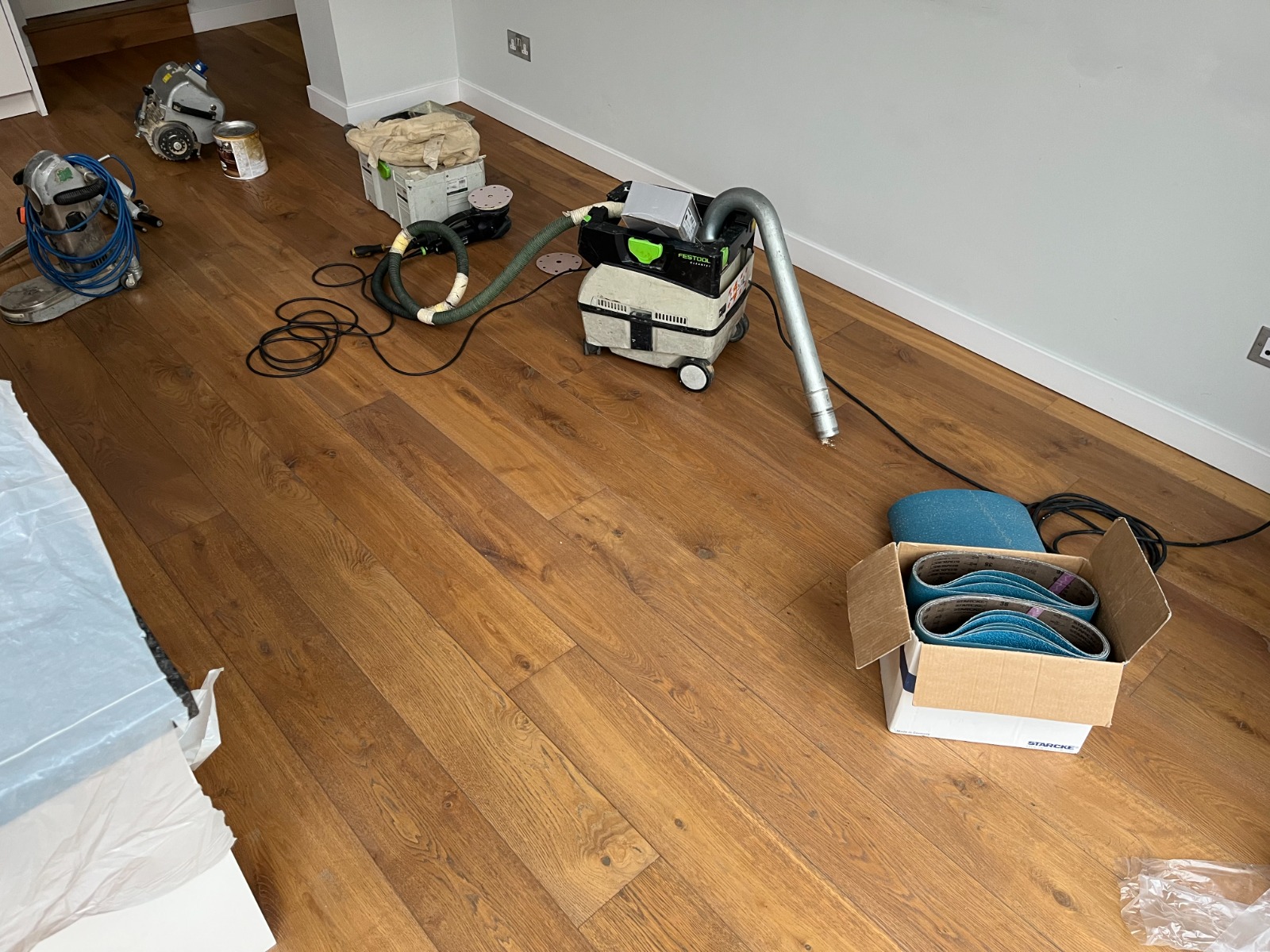 Dust-free sanding setup on an engineered oak plank floor in West Brompton, with belt sander, edger, extractor and abrasives staged for creak-fix prep — Squeaky Repairs Revealed.