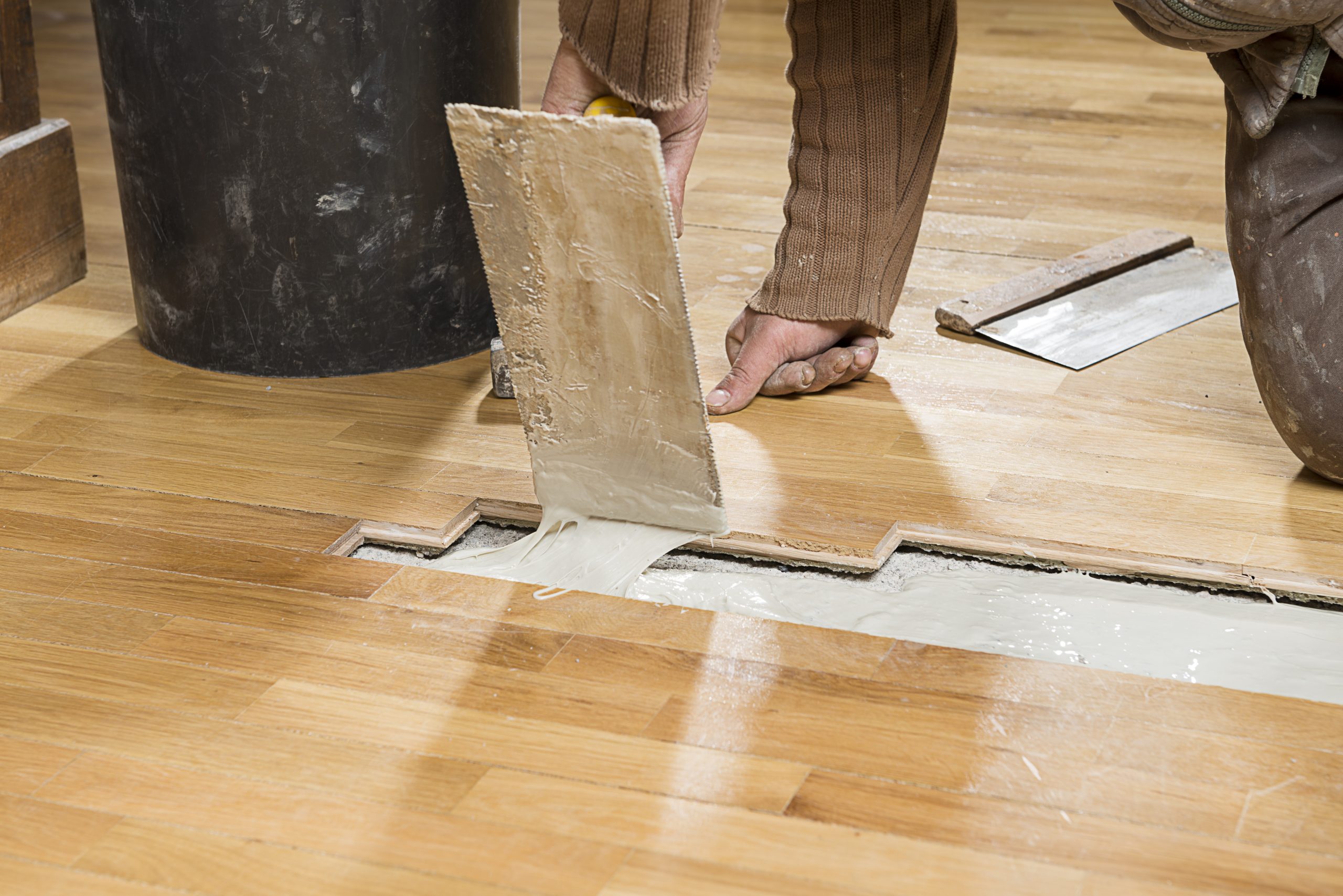 West Brompton oak parquet wood block floor during repair—loose blocks lifted and MS polymer adhesive trowelled into the subfloor channel to re-bond and silence creaks — Squeaky Repairs Revealed.