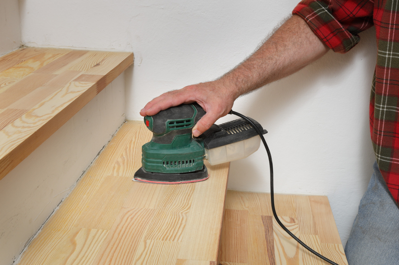 Close-up of a pine softwood staircase in West Brompton: a technician sands the stair tread with a detail sander after tightening fixings to stop creaks — Squeaky Repairs Revealed.