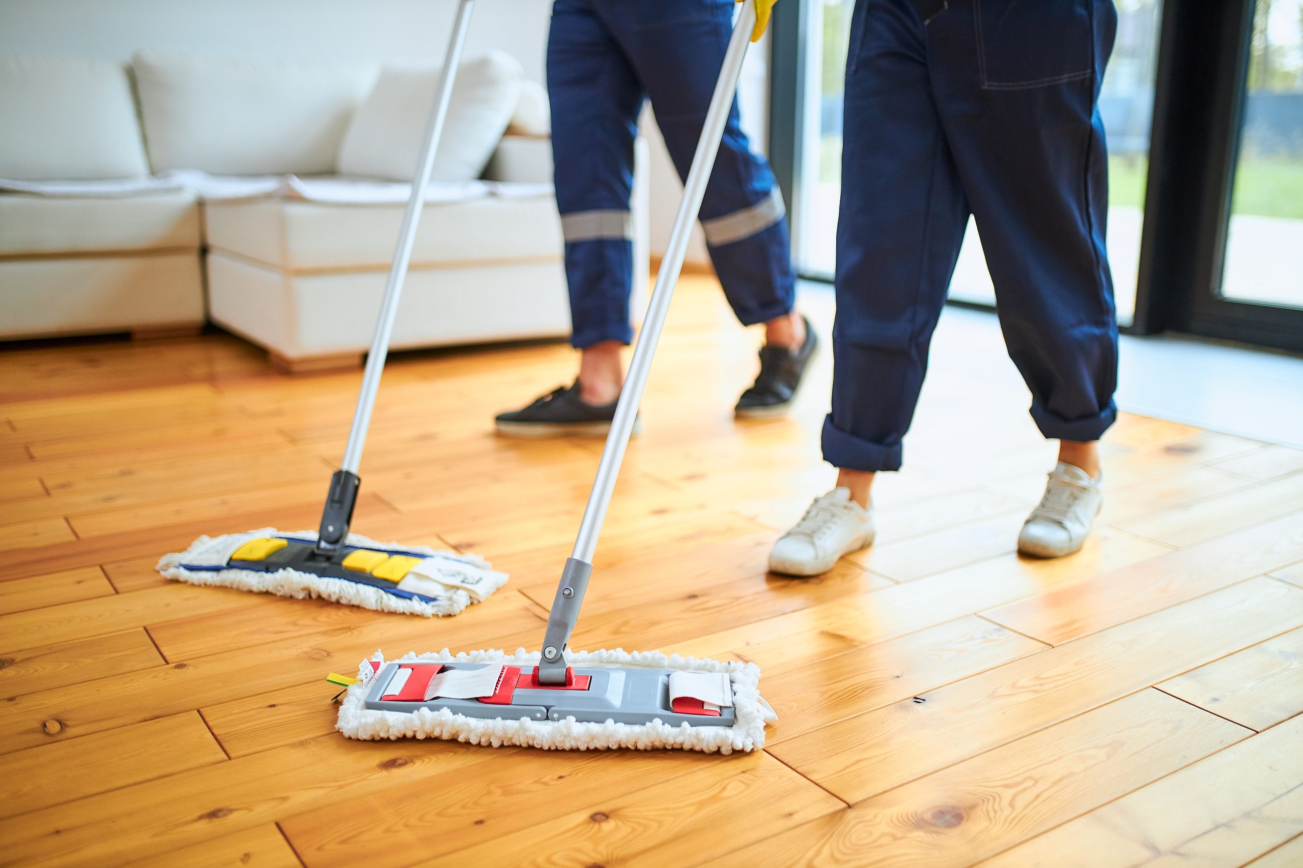 After Wood Floor Sanding in West Brompton, two cleaners mop a freshly restored oak hardwood floor in a bright living room.