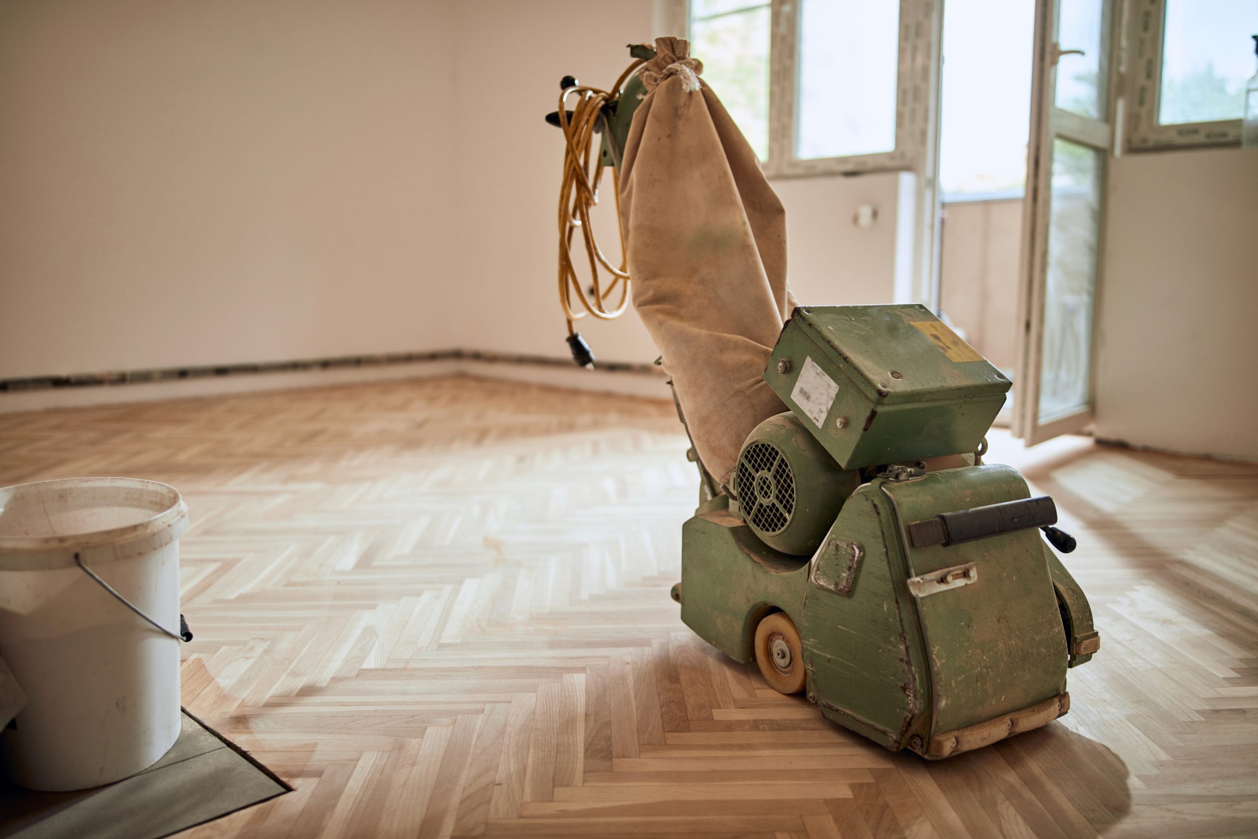 Wood Floor Sanding in West Brompton on light oak herringbone parquet flooring with a professional belt sander in an empty room.