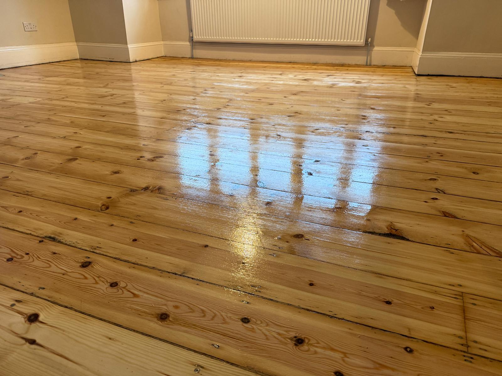 Wood Floor Sanding in West Brompton on varnished pine softwood floorboards, showing a smooth, glossy finish across a bright room.