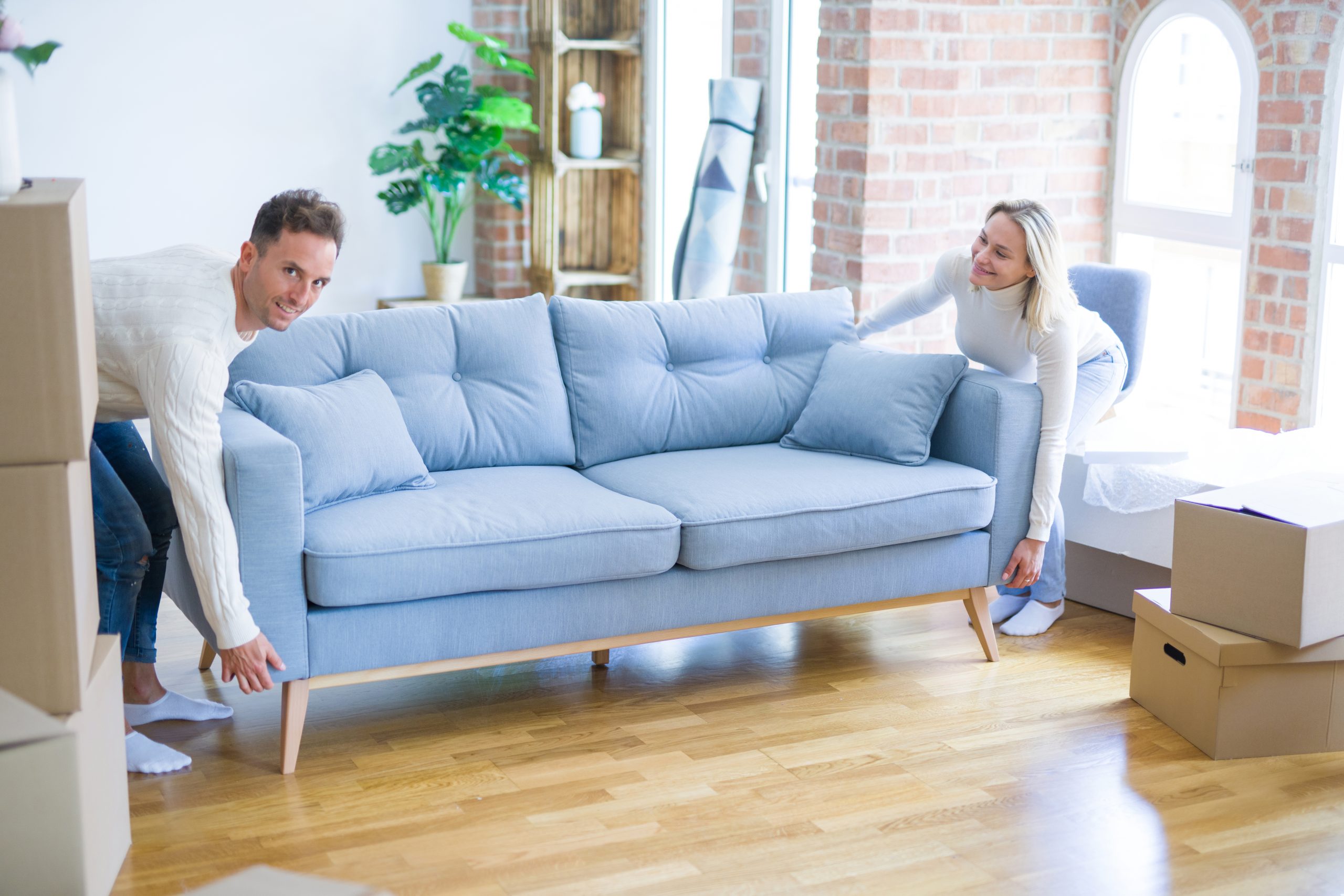 Couple moving a blue sofa in a bright West Brompton living room with freshly restored oak hardwood floor after professional Hardwood Floor Sanding.