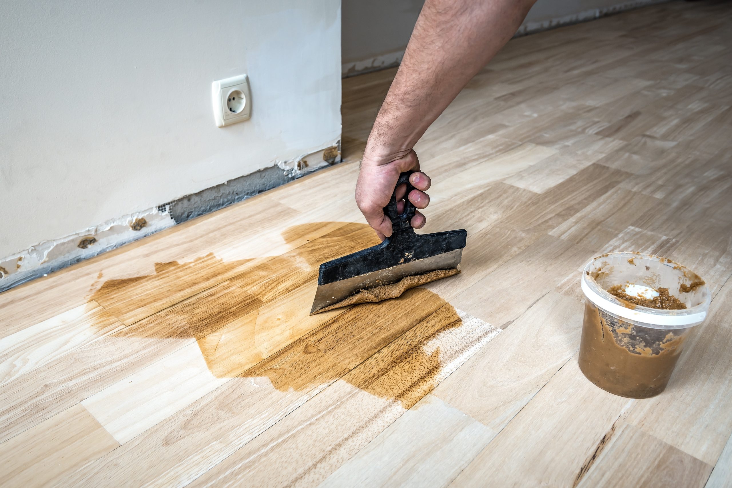 Hardwood Floor Sanding in West Brompton on an oak plank hardwood floor, showing a technician spreading resin filler to gap-fill the boards before refinishing.