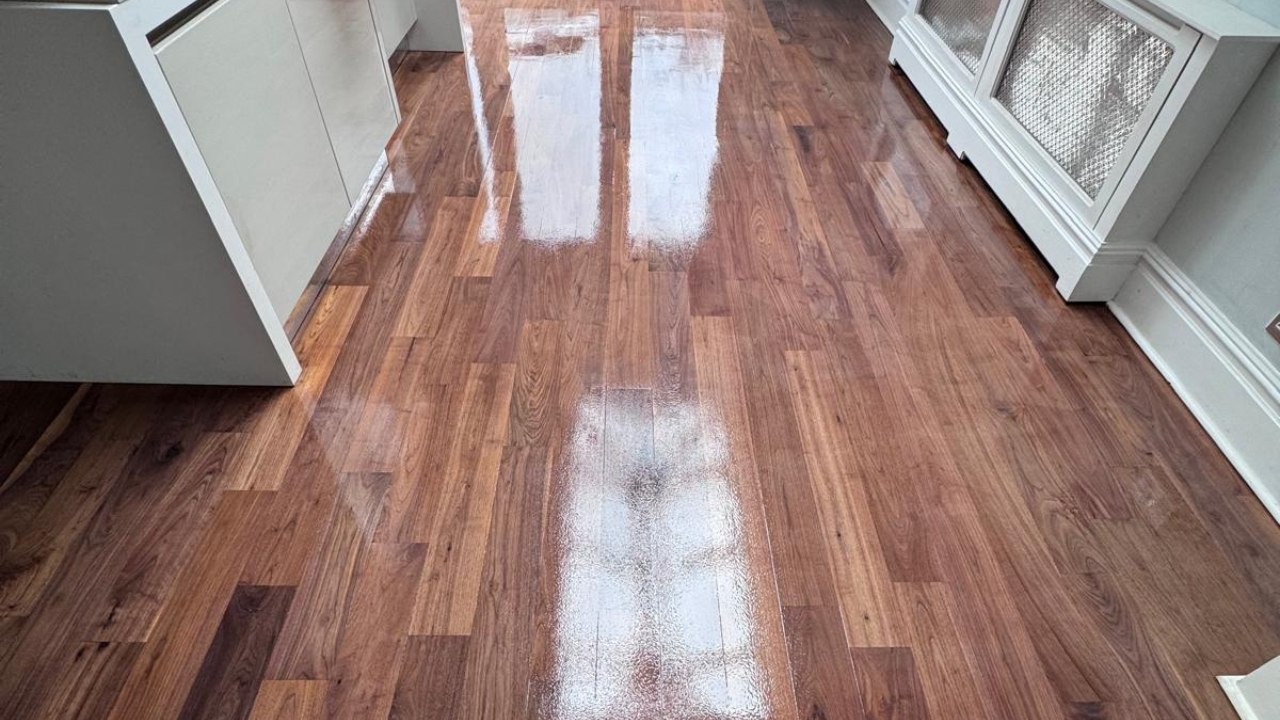 Hardwood Floor Sanding in West Brompton on a walnut plank hardwood kitchen floor, showing a rich, glossy finish with window light reflecting across the boards.